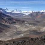 南極大陸の氷のない渓谷(ドライバレー)を写した風景写真。荒涼とした岩と土壌が広がり、遠くに雪山が見える。